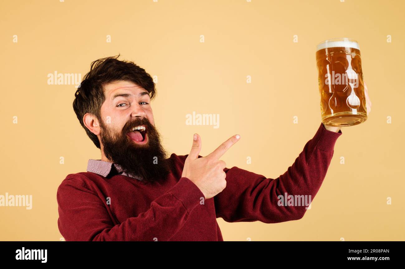 Ein bärtiger Mann, der mit dem Finger auf einen Craft-Bier-Becher zeigt. Brauereikonzept. Fröhliche Brauerin mit einem Becher Ale. Bierkneipe oder Bar. Ein Mann, der Bier vom Fass probiert. Fröhliches Lächeln Stockfoto