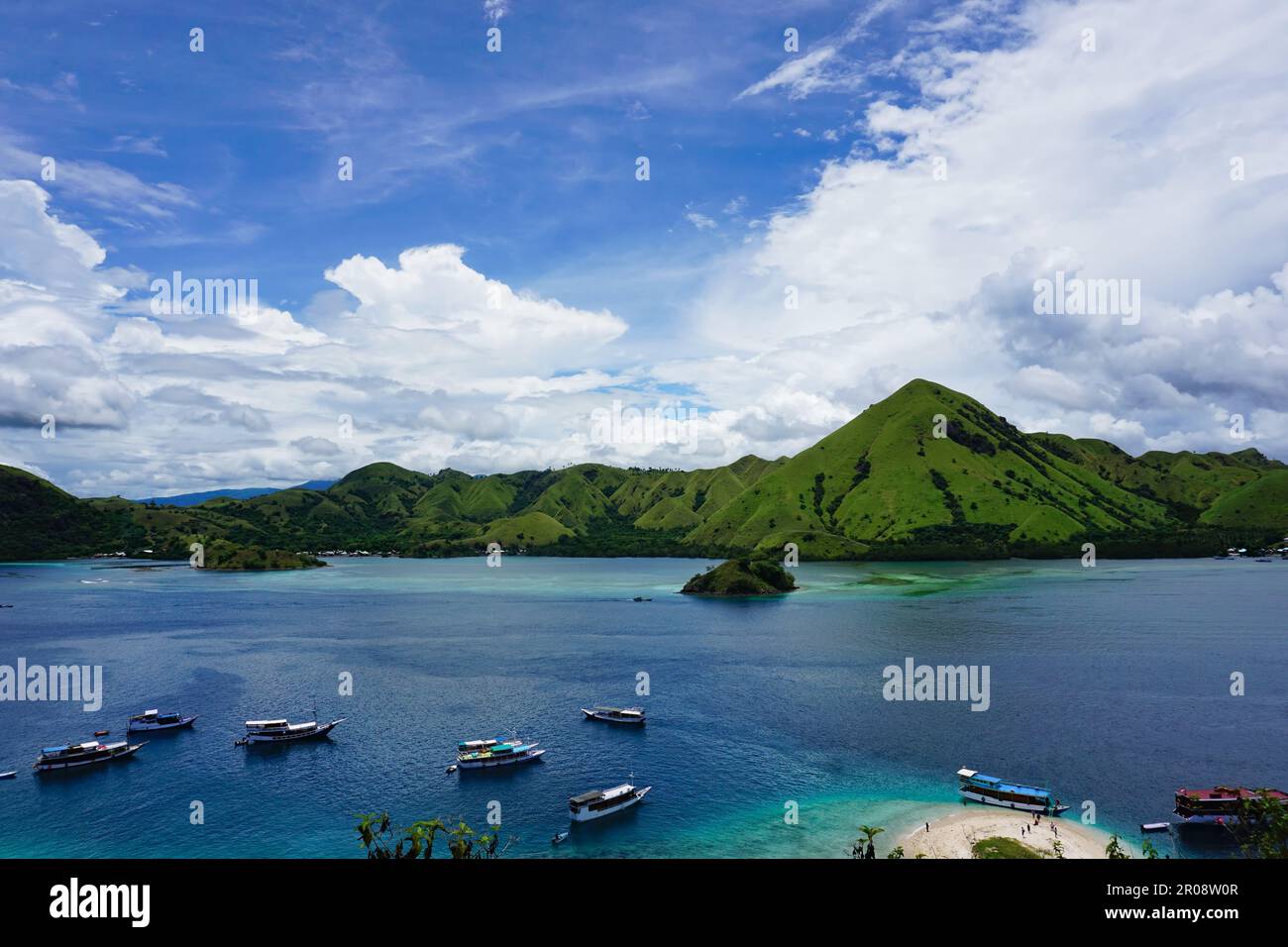 Boote ankern im blauen türkisfarbenen Wasser vor einer Insel, Komodo Nationalpark, Indonesien, Küstendorf im Hintergrund Stockfoto