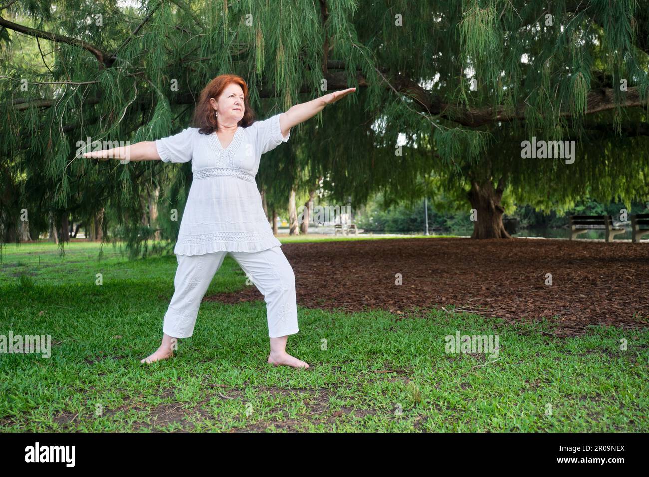 Porträt einer erwachsenen hispanischen Frau in weißer Kleidung, die im Park Yoga praktiziert. Konzepte: Wellness, Vitalität, aktiver und gesunder Lebensstil. Stockfoto