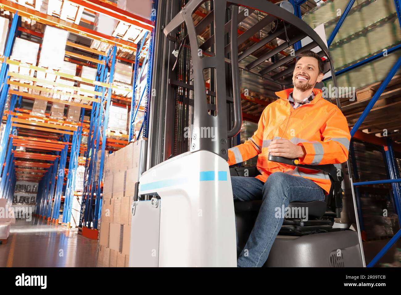 Glücklicher Arbeiter, der im Gabelstapler im Lager sitzt Stockfoto