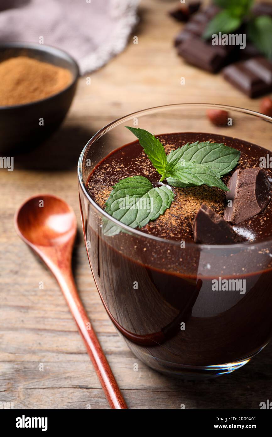 Ein Glas köstliche heiße Schokolade mit frischer Minze und Löffel auf einem Holztisch Stockfoto