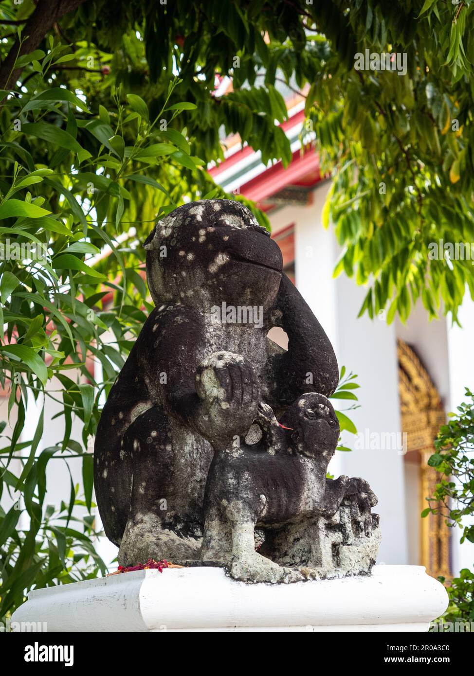 Eine fröhliche Affenstatue lächelt inmitten des Grüns vor dem Wat Pho Tempel, einem buddhistischen kulturellen Wahrzeichen in Bangkok, Thailand. Stockfoto