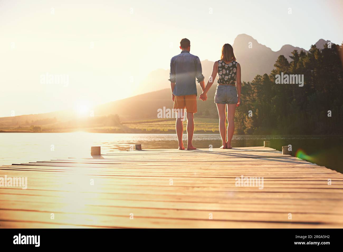Liebe unter einem wunderschönen Sonnenuntergang. Rückblick auf ein liebevolles junges Paar, das bei Sonnenuntergang auf einem Dock steht. Stockfoto