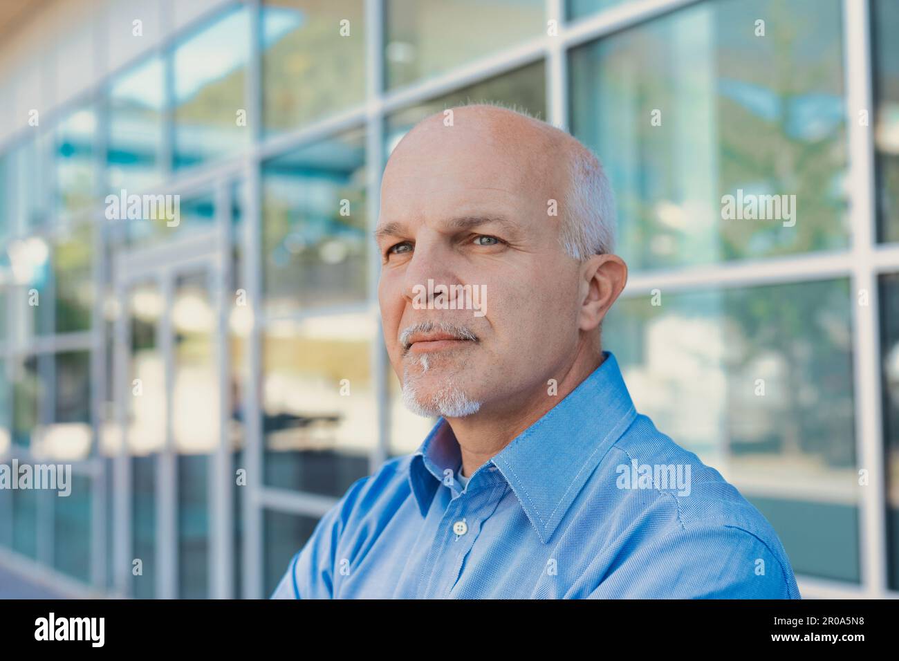 Ein Mann mittleren Alters in der Nähe eines hochmodernen, aus Stahl und Glas bestehenden Gebäudes scheint mit einem leichten Lächeln auf den Akt zu warten oder ihn zu beobachten Stockfoto