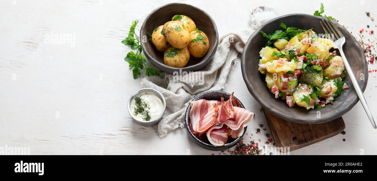 Schüssel mit warmem Kartoffelsalat mit Speck auf weißem Hintergrund. Draufsicht. Panorama mit Kopierbereich. Stockfoto
