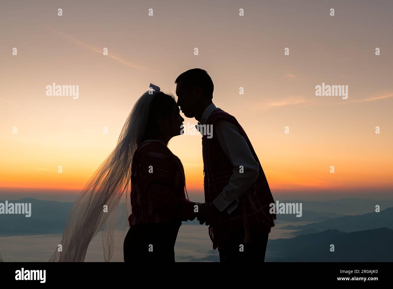 Silhouette eines verliebten Ehepaars, das sich küsst und bei Sonnenaufgang Hand an Hand hält, mit morgendlichem Himmelshintergrund Stockfoto