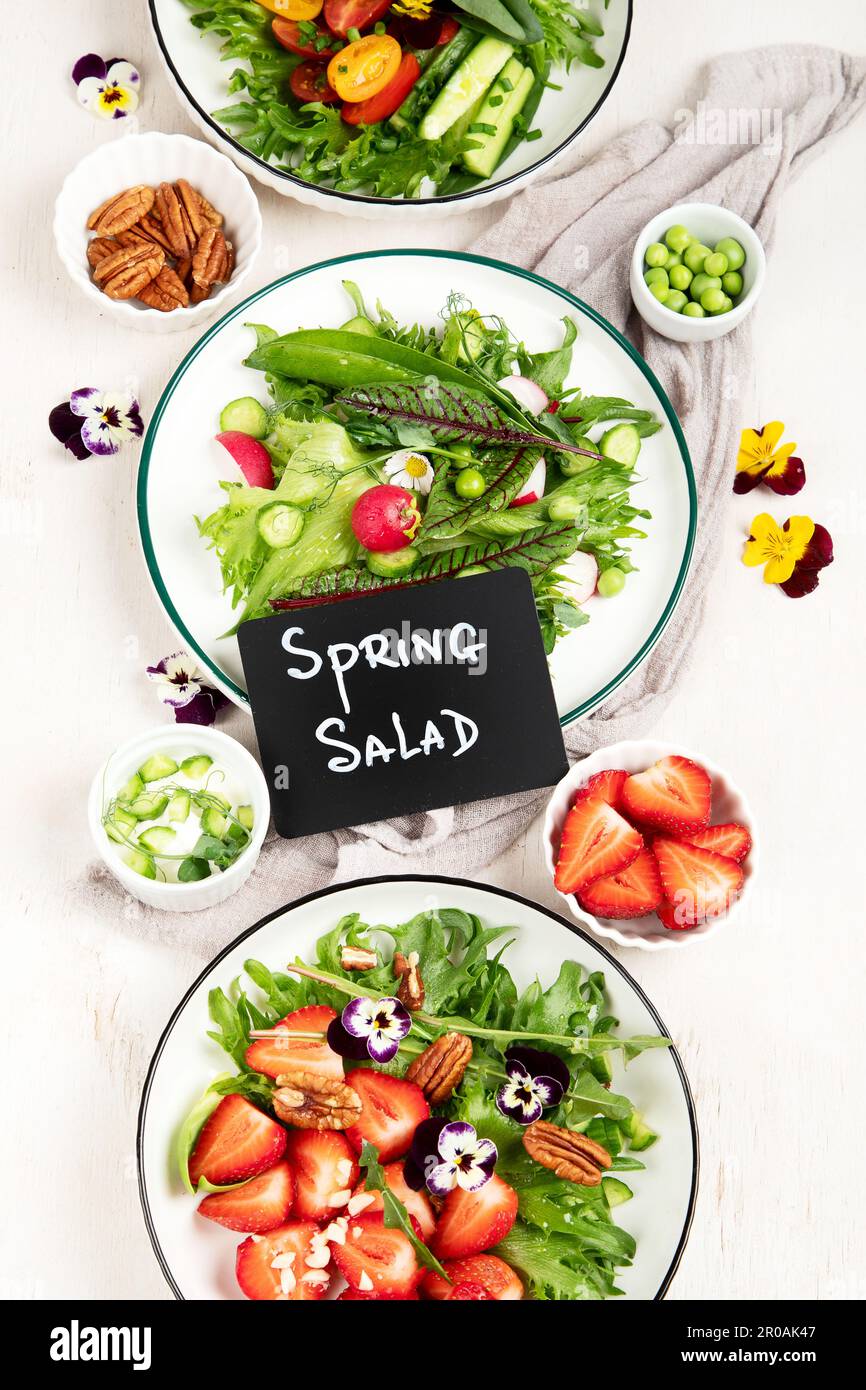 Köstliche Frühlingssalate mit essbaren Blumen, Gemüse, Obst, Mikrogreens und Käse auf weißem Hintergrund. Konzept der sauberen und gesunden Ernährung. Oben vi Stockfoto