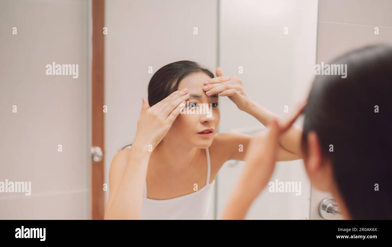 Schönheit in Spiegelreflexion. Über der Schulter des Gesichts einer schönen Frau, die ihr Gesicht berührt, während sie in den Spiegel schaut Stockfoto