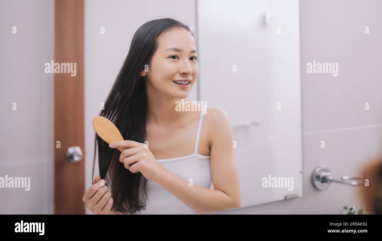 Fröhliche, attraktive junge Frau, die nach der Dusche zuhause nasses Haar mit Kamm im Bad kämmt. Haarpflege und gesundes Haar Stockfoto