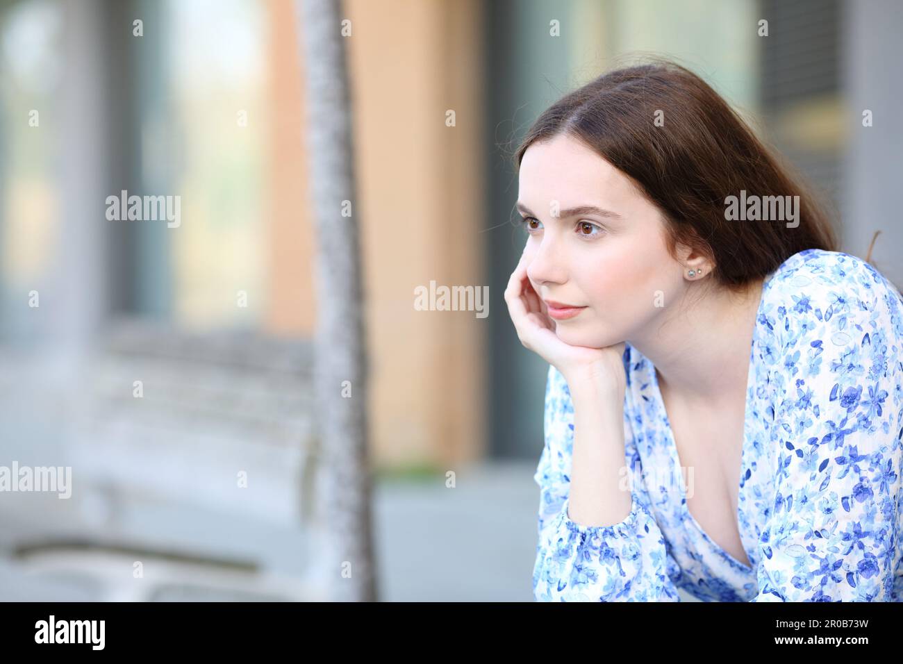 Eine nachdenkliche Frau, die denkt, allein auf der Straße zu sitzen Stockfoto