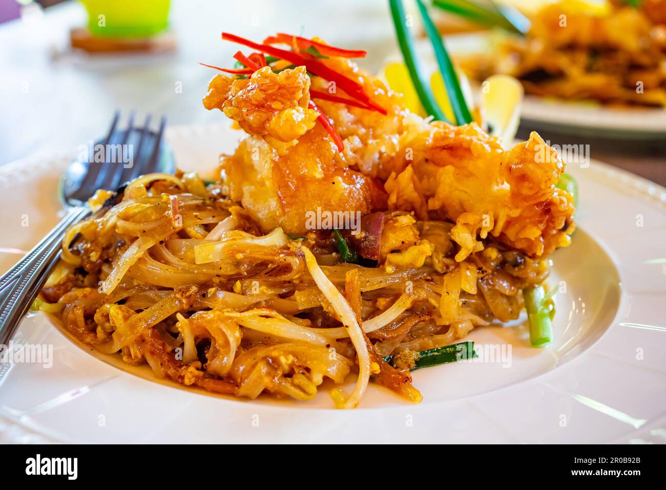 Pad thai-Reisnudeln mit frittierten Garnelen oder Garnelen und Gemüse in weißer Keramikplatte auf Holztisch. Stockfoto