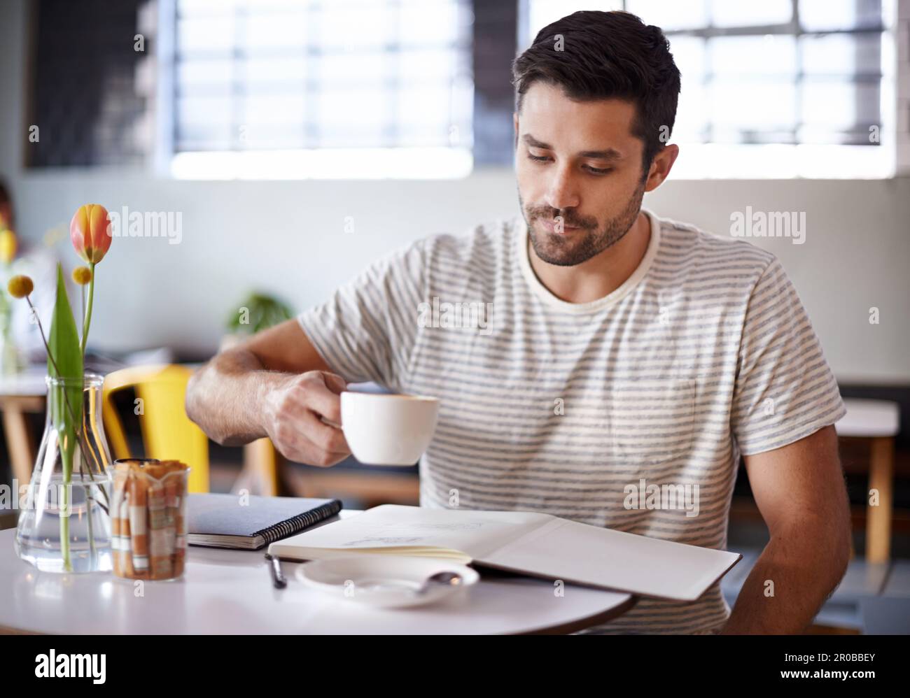 Zeit, sich zu konzentrieren. Ein gutaussehender junger Mann, der Kaffee trinkt, während er mit seinem Notizbuch in einem Restaurant sitzt. Stockfoto