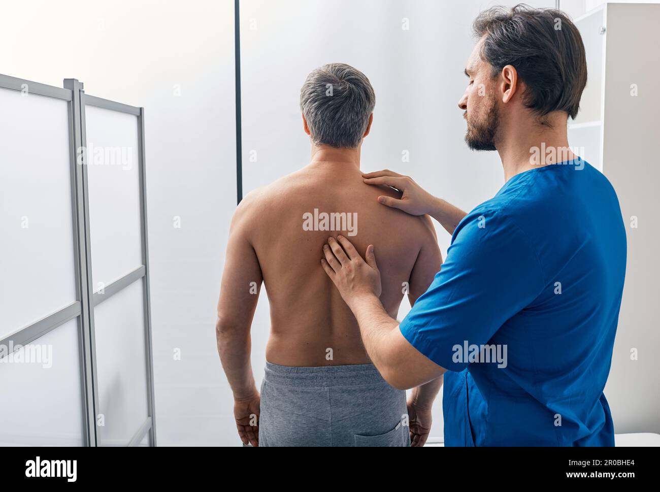 Der stehende männliche Patient lässt seine Wirbelsäule mit Osteopath untersuchen. Osteopathen-Untersuchung Stockfoto