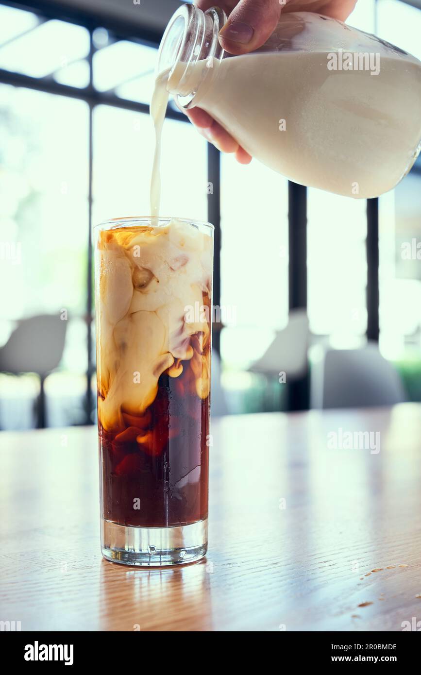 Kalter Kaffee, der auf einem Holztisch mit dicker Sahne aufgefüllt wird. Stockfoto