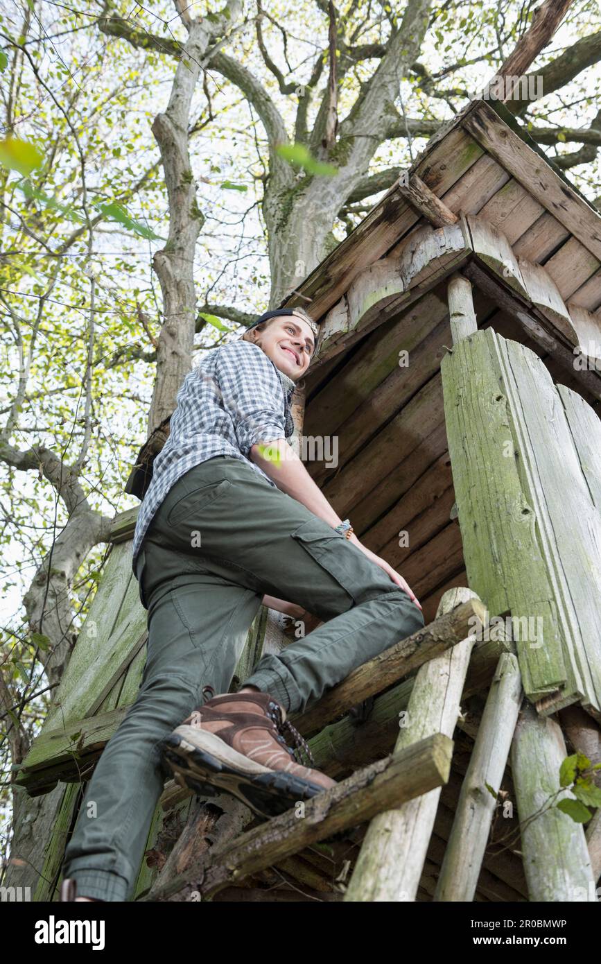Blick aus dem niedrigen Winkel auf einen männlichen Wanderer im Teenageralter, der auf den Aussichtsturm im Wald in Bayern klettert Stockfoto