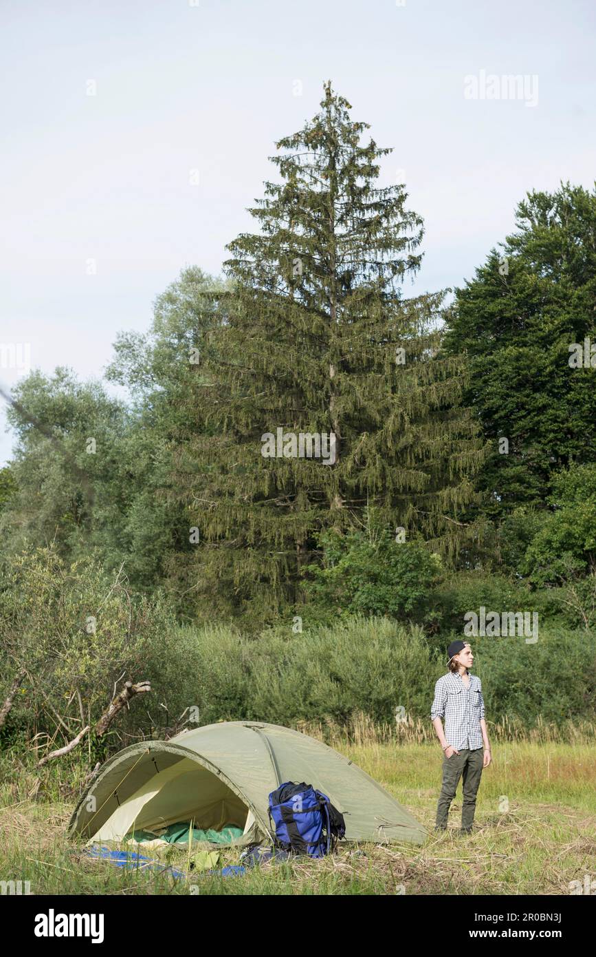 Ein Teenager, der neben seinem Zelt steht, im Wald, Bayern, Deutschland Stockfoto
