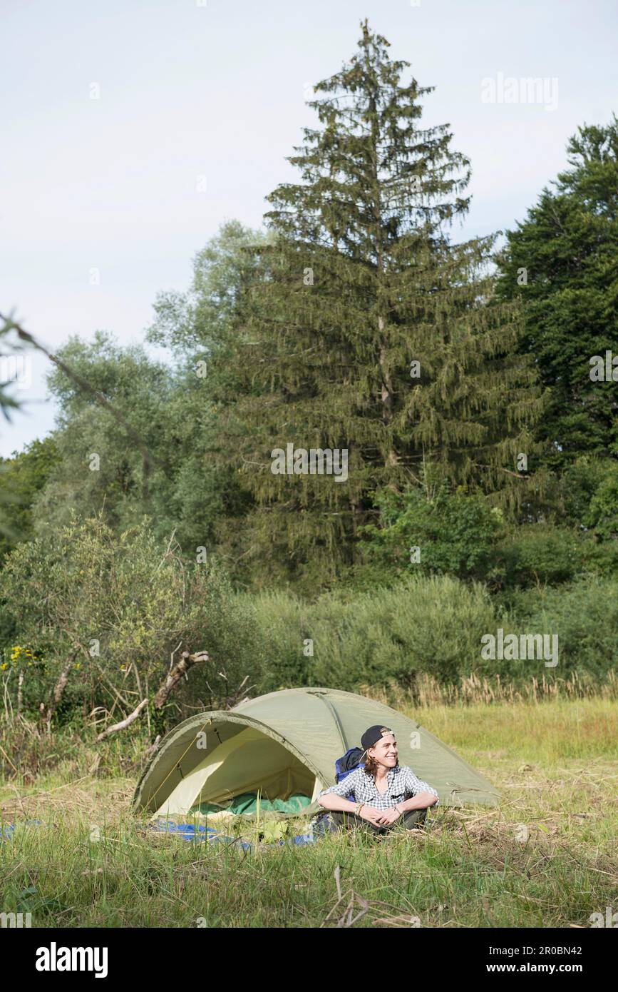 Ein Teenager sitzt neben seinem Zelt im Wald, Bayern, Deutschland Stockfoto