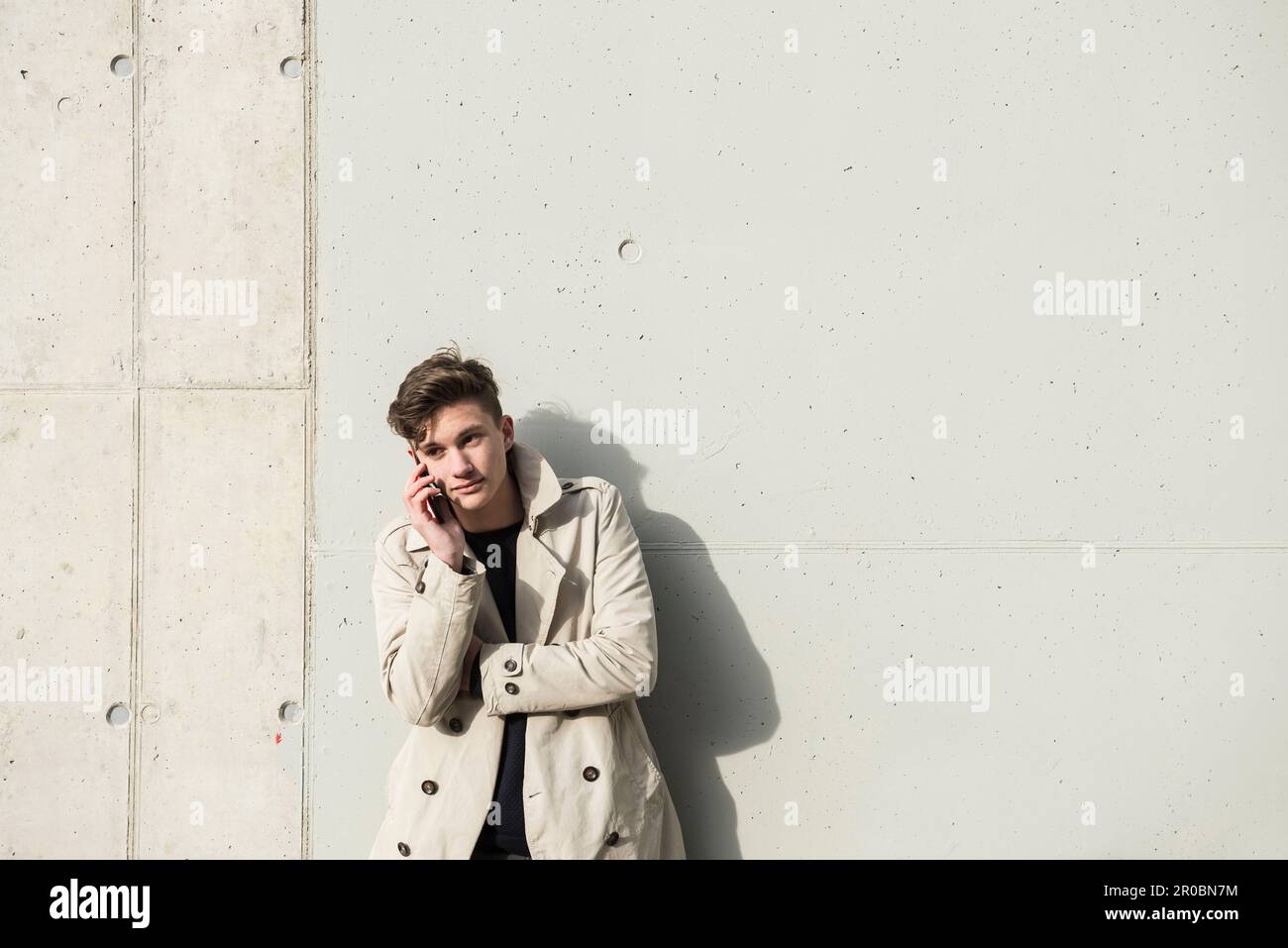 Junger Mann, der mit dem Handy spricht und sich an die Betonwand lehnt, München, Bayern, Deutschland Stockfoto
