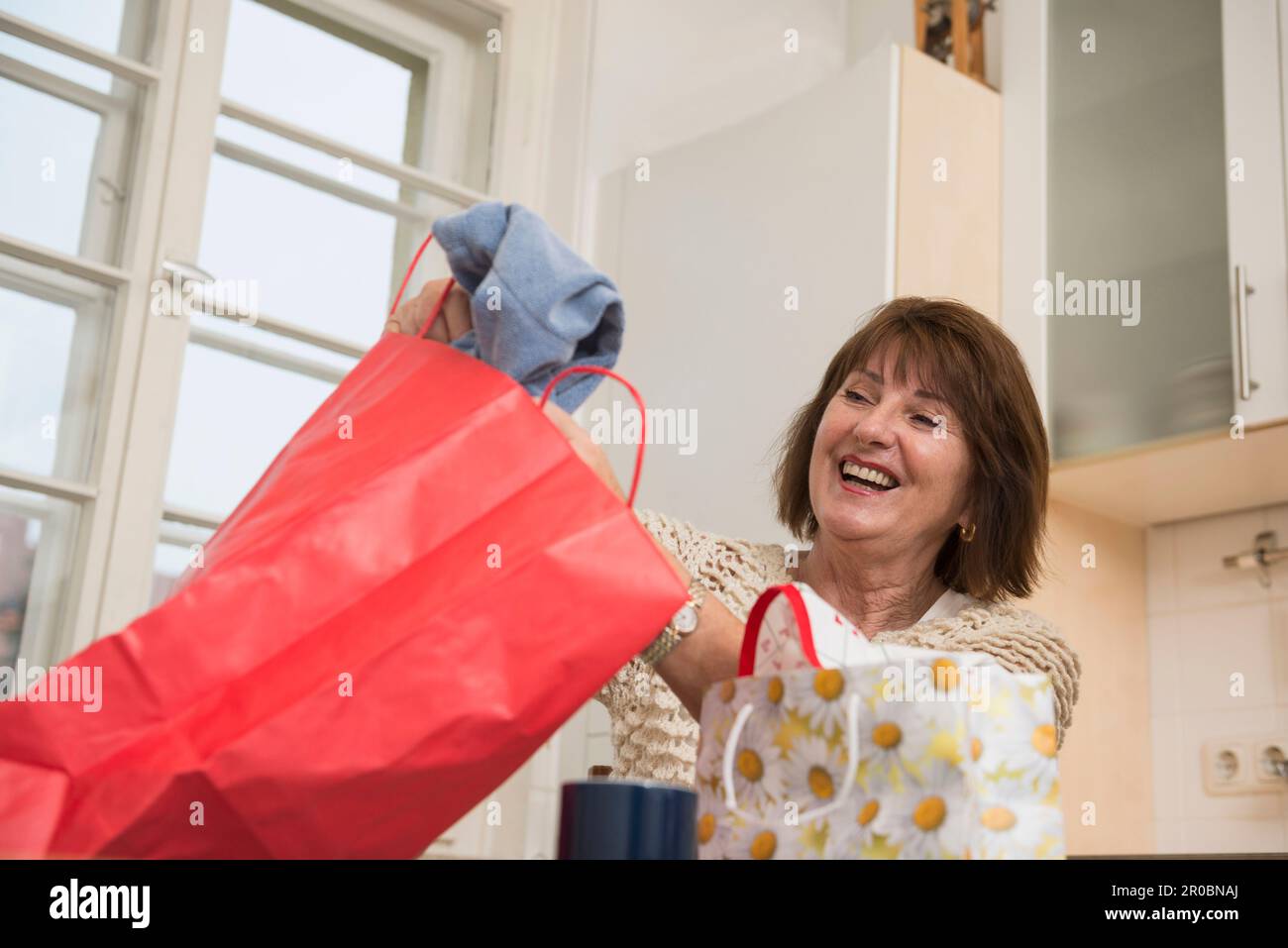 Seniorin, die in die Einkaufstasche schaut und in der Küche lächelt, München, Bayern, Deutschland Stockfoto