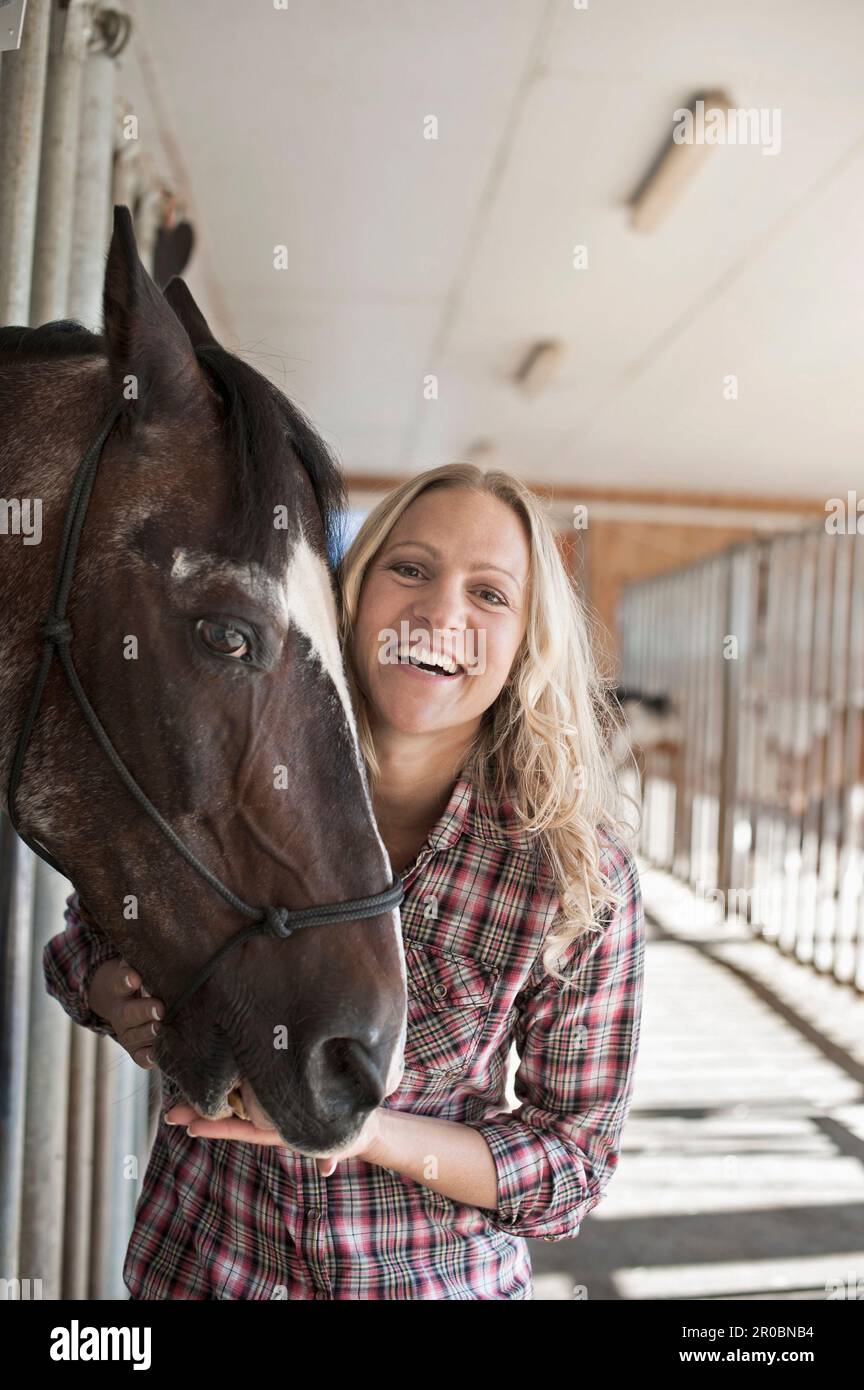 Porträt einer erwachsenen Frau mit ihrem Pferd in der Scheune und lächelnd, Bayern Stockfoto