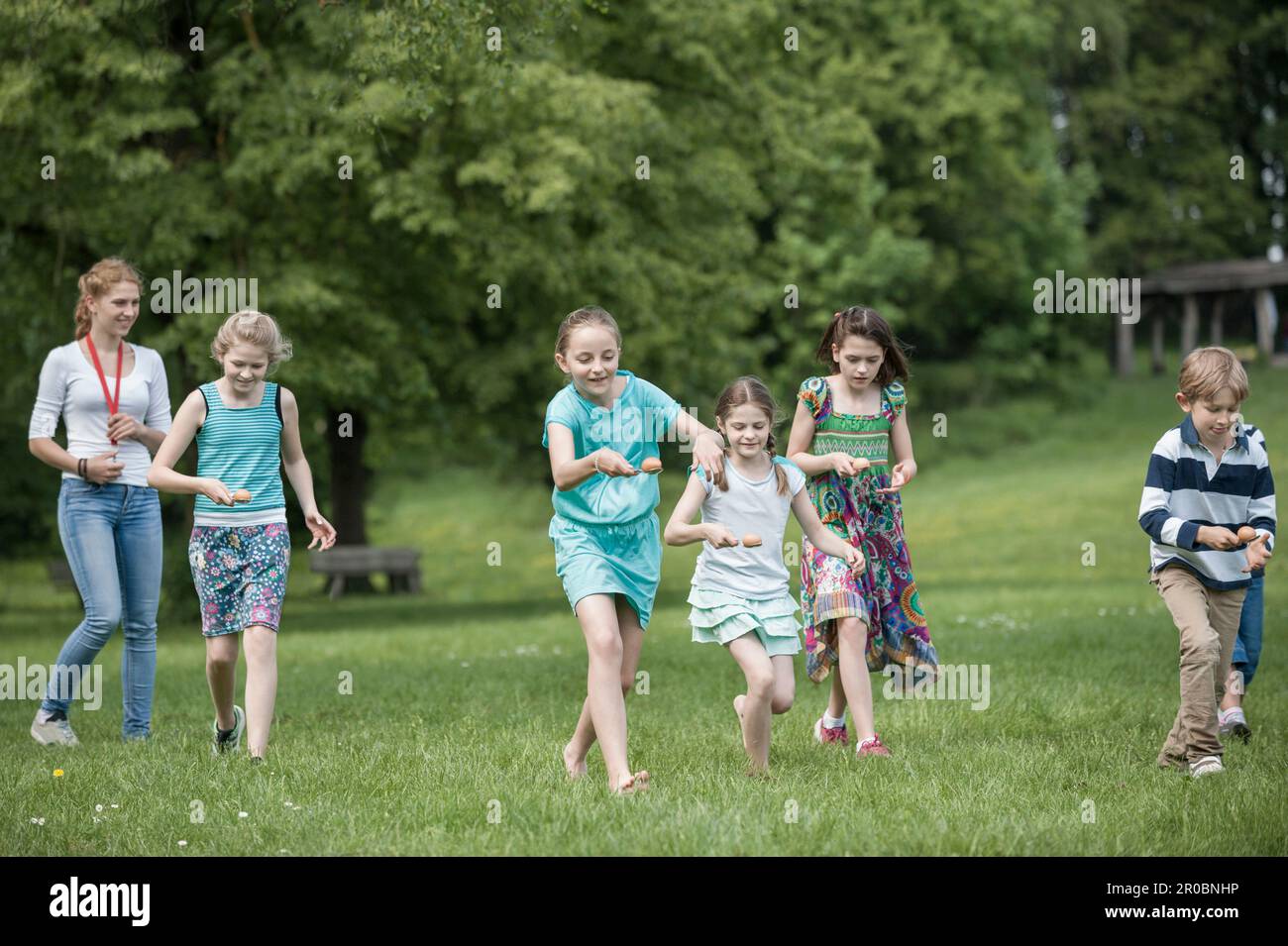 Gruppe von Kindern, die an einem Ei-Löffel-Rennen im Park, München, Bayern teilnehmen Stockfoto