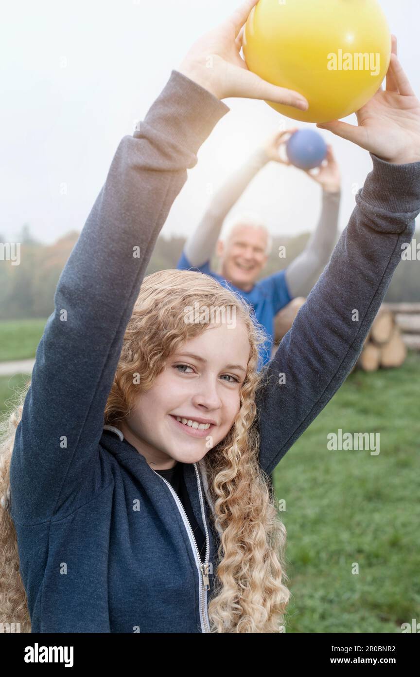 Teenage Girl mit ihrem Vater, der Yoga-Ball auf dem Feld trainiert und in der Morgendämmerung lächelt, Bayern, Deutschland Stockfoto