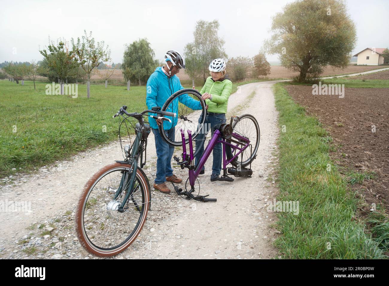 Seniorenpaar, das das Rad des Fahrrads auf der Landstraße justiert, Bayern, Deutschland Stockfoto