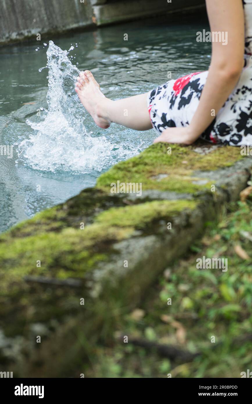 Eine Frau, die Wasser mit ihrem Bein am Eisbach-Flussufer spritzt Stockfoto