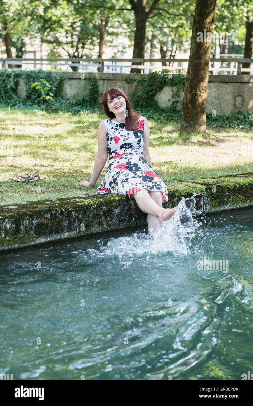 Schöne Frau, die Wasser mit ihren Beinen am Eisbach-Flussufer spritzt Stockfoto