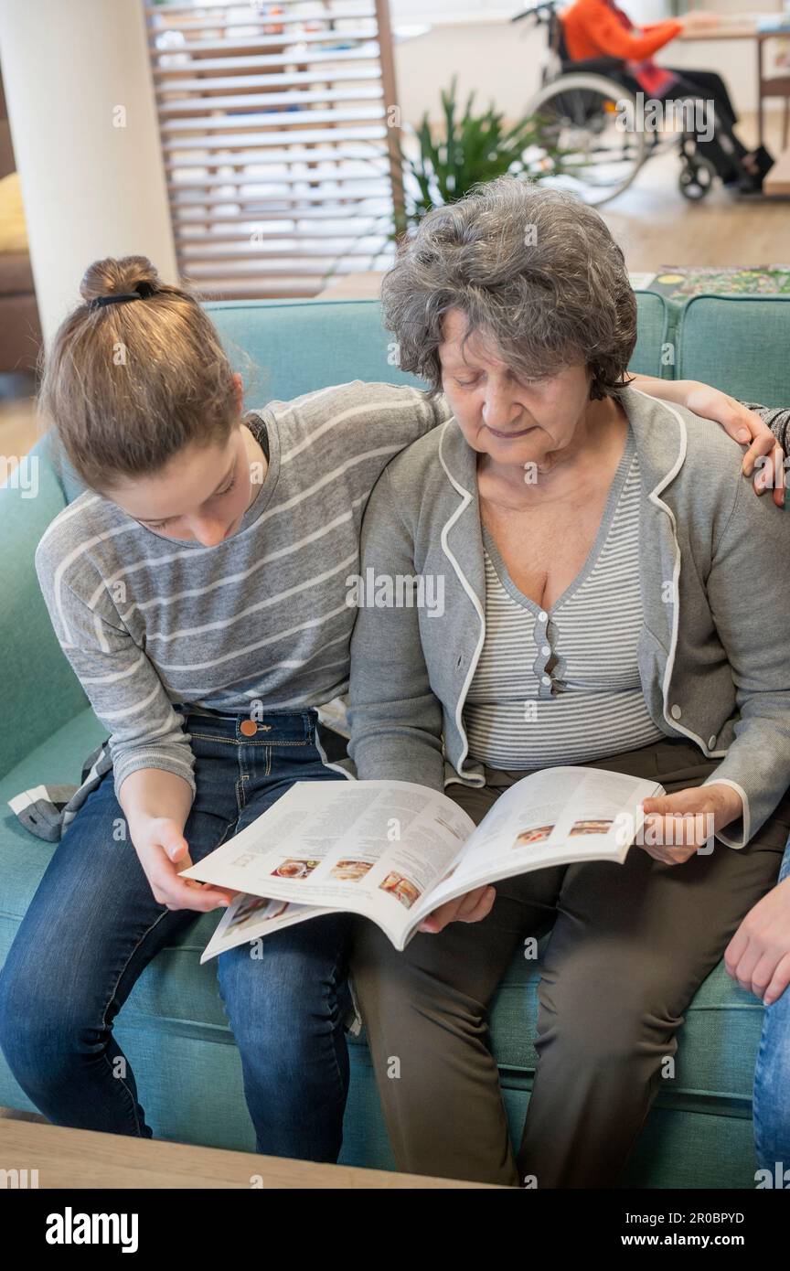 Mädchen lesen Zeitschrift mit Seniorin im Altersheim Stockfoto