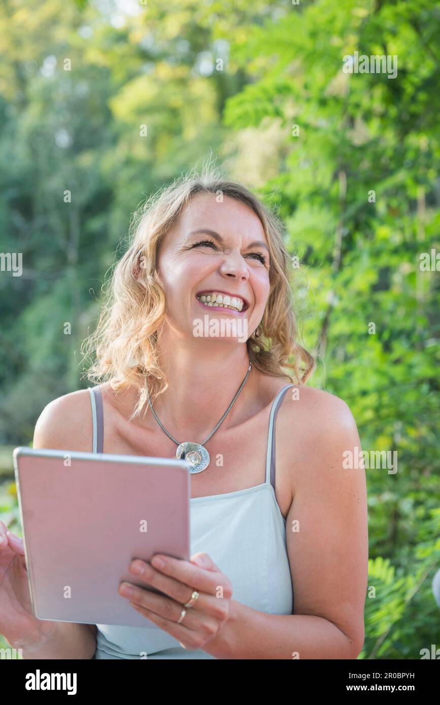 Schöne lächelnde Frau, die ein digitales Tablet in der Natur verwendet Stockfoto