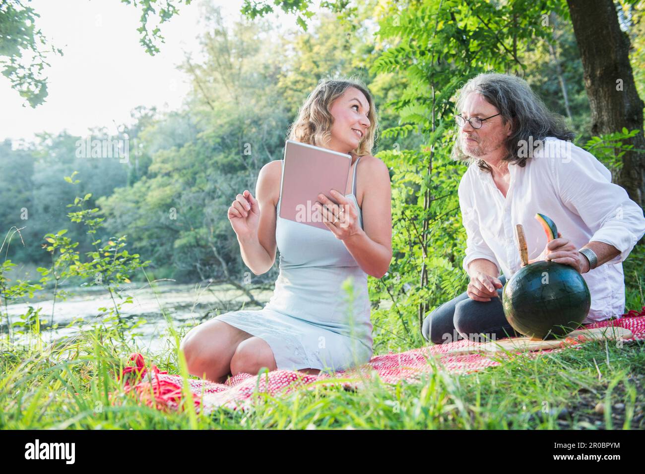 Ein Paar auf einem Picknick mit Tablet, isst Wassermelone am See, Bayern, Deutschland Stockfoto