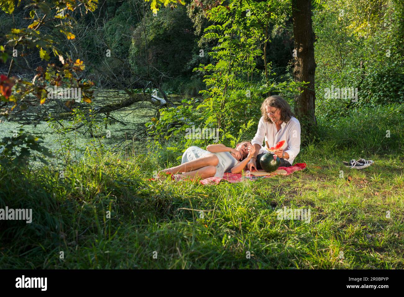 Ein Paar, das ein Picknick macht und Wassermelone am Flussufer in Bayern isst Stockfoto