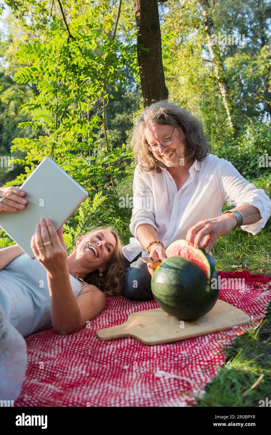 Ein Paar auf einem Picknick mit Tablet und Wassermelone schneiden, Bayern, Deutschland Stockfoto