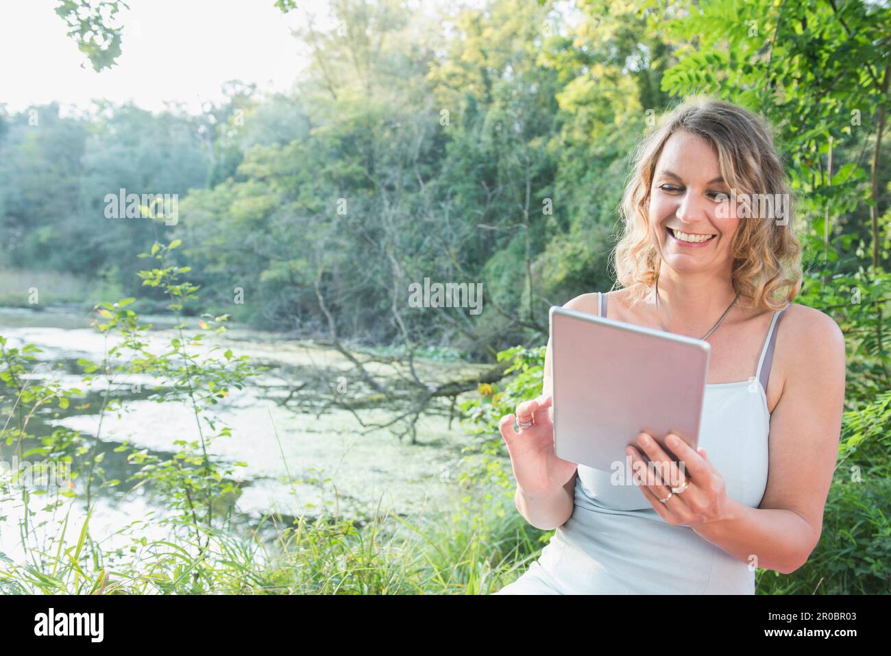 Schöne Frau, die ein digitales Tablet benutzt, am See, Bayern, Deutschland Stockfoto