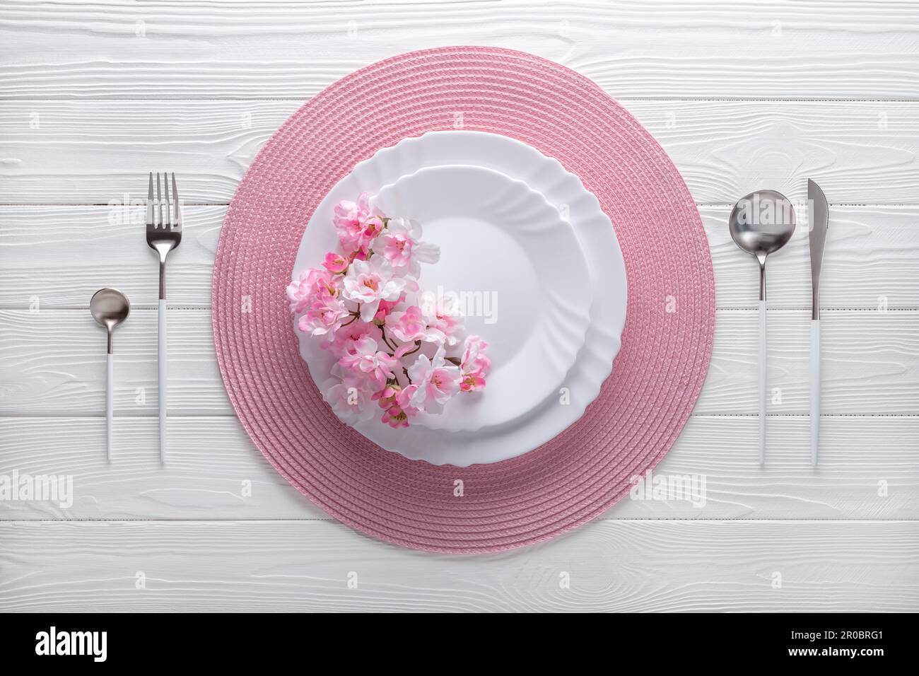 Festlicher Ort mit pinkfarbener Serviette und Frühlingsblumen. Leere Teller und silbernes Besteck auf weißem Holztisch. Draufsicht. Festliches Abendessen im luxuriösen Stockfoto
