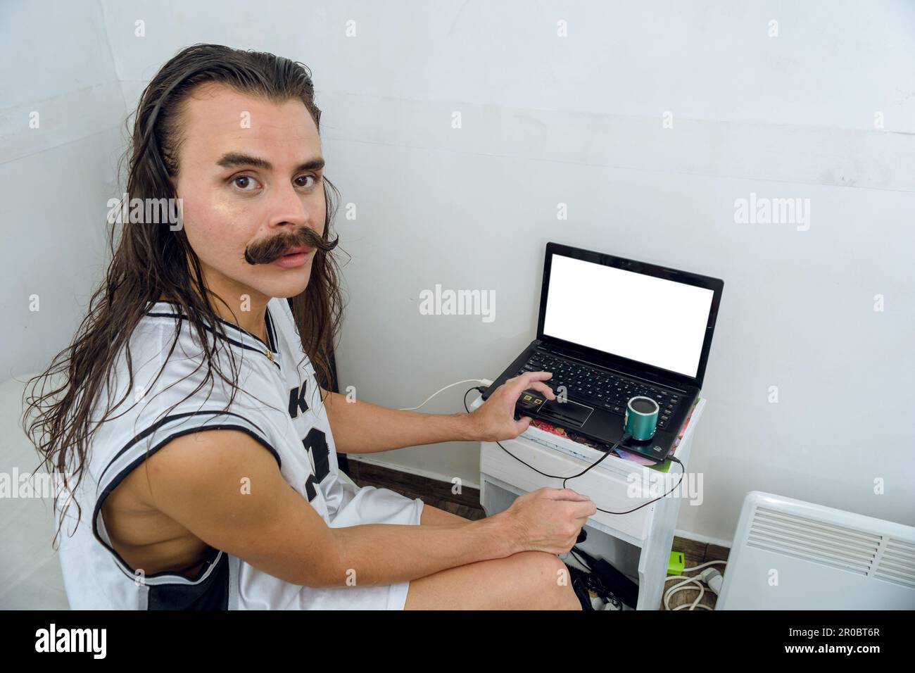 Junge, nicht binäre Latino-Person, die auf dem Bett in ihrem Zimmer sitzt, den Laptop benutzt und ernsthaft in die Kamera schaut, Lifestyle-Konzept, Copy Spa Stockfoto