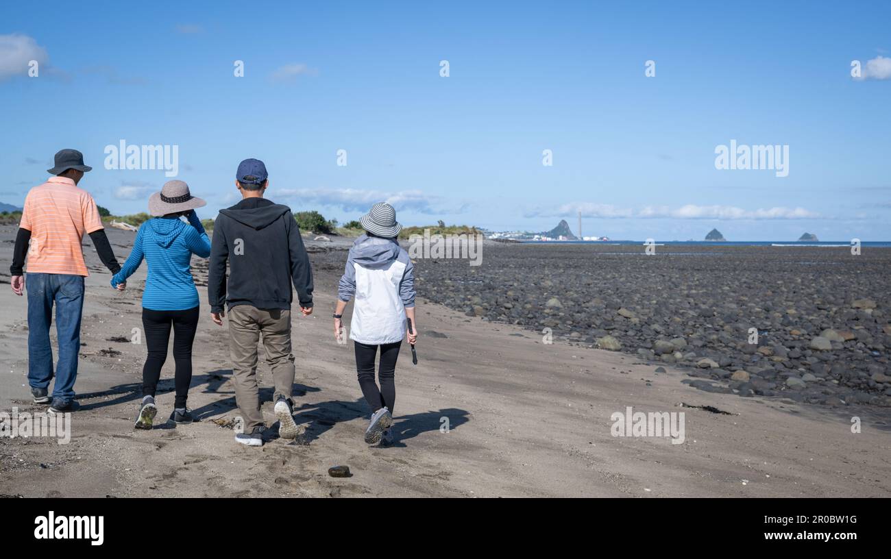 Vier Leute laufen am Strand. Zuckerlaafinseln in der Ferne. Touristen amüsieren sich. Neuer Plymouth. Stockfoto