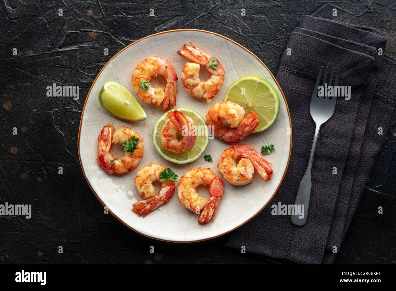 Shrimps, Kopfschuss. Gebratene Garnelen mit Limette auf einem Teller, von oben auf schwarzem Steinhintergrund geschossen Stockfoto