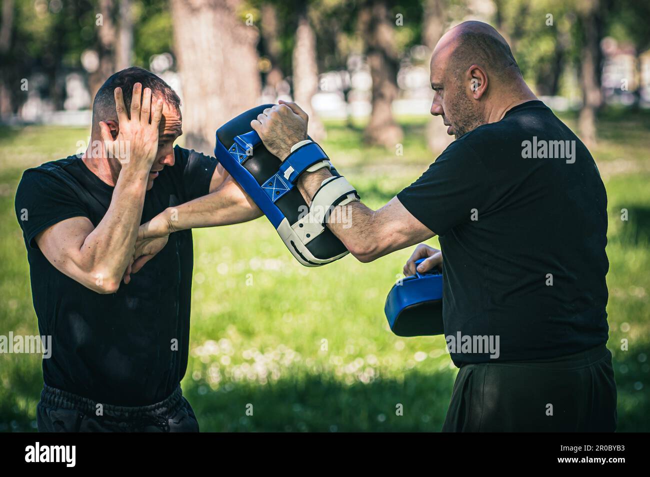 Muay thai-Trainer hält fokussierte Handschuhe. Ellenbogen-Kick-Technik-Training und Demonstration mit Pads. Kampfsportübungen Stockfoto