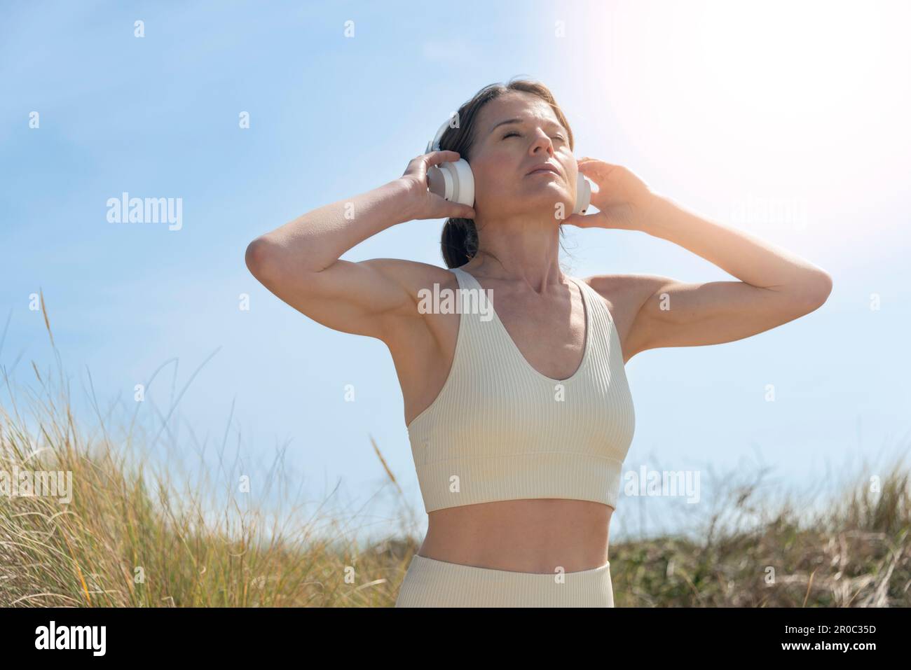 Sportliche Frau, die beim Training in der Sonne die Hämophonsteine auf dem Kopf hält Stockfoto