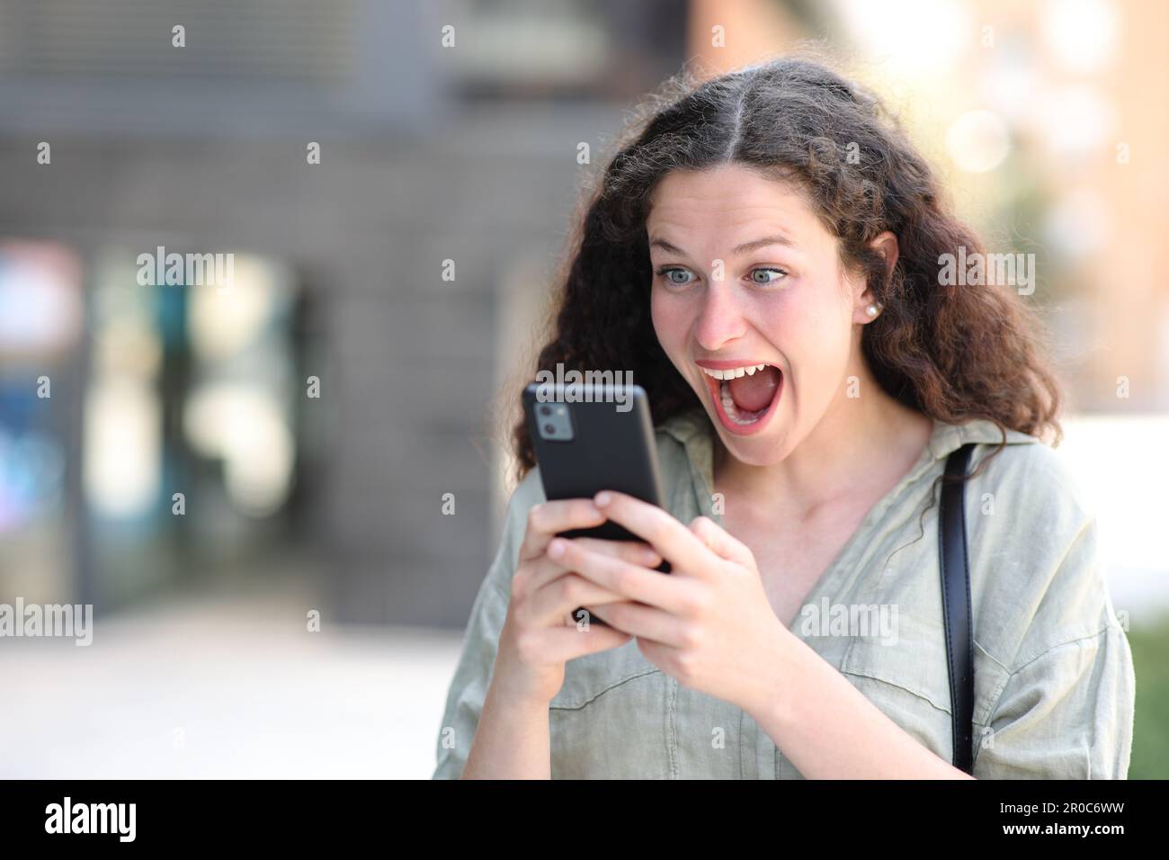 Aufgeregte Frau, die auf der Straße unterwegs auf dem Telefon fantastische Inhalte ansieht Stockfoto