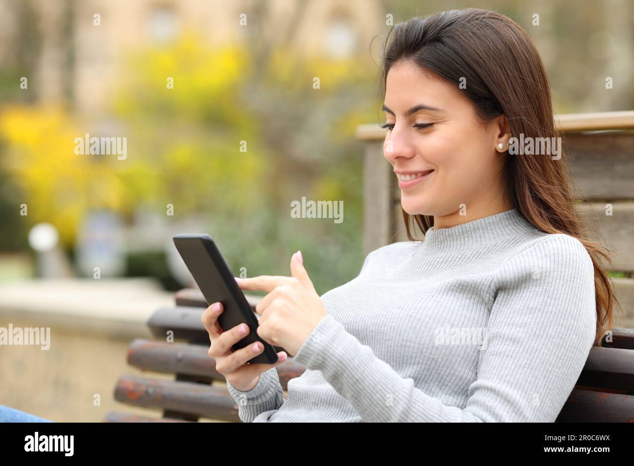 Glücklicher Teenager, der sein Smartphone benutzt und auf einer Bank im Park sitzt Stockfoto