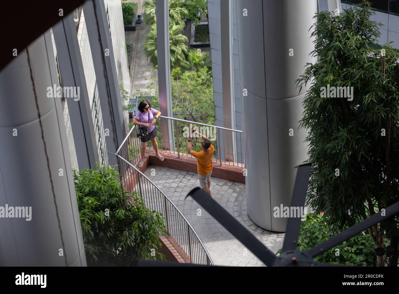 Aus der Vogelperspektive, von oben nach unten, ein Mann fotografiert eine Frau, die am Felsvorsprung posiert. CapitaSpring, Singapur. Stockfoto