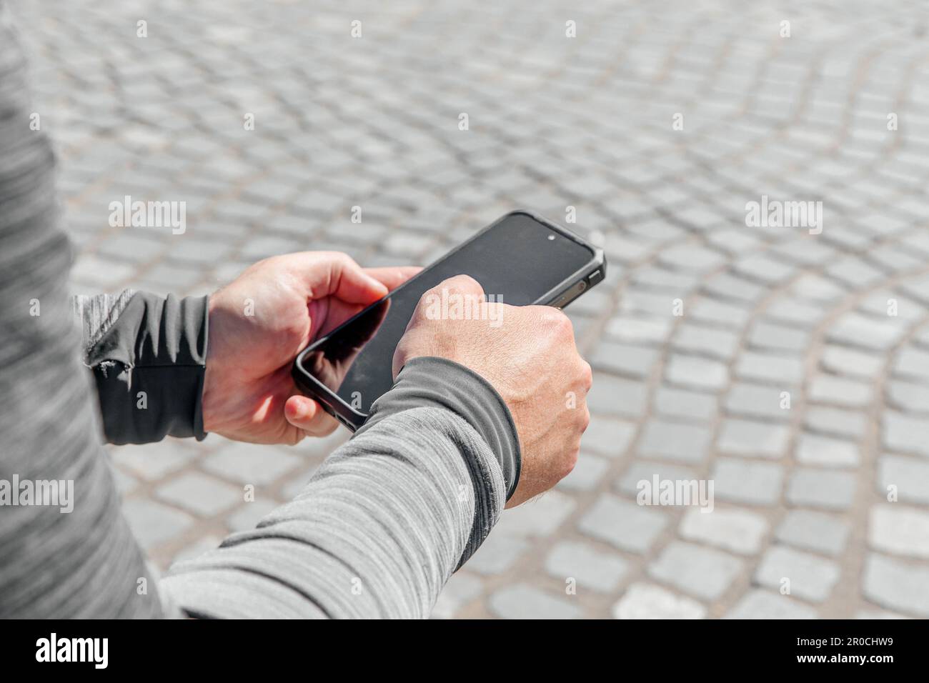 Ein Mann mit einem Smartphone in der Hand sitzt mitten in der Stadt bei Tageslicht Stockfoto