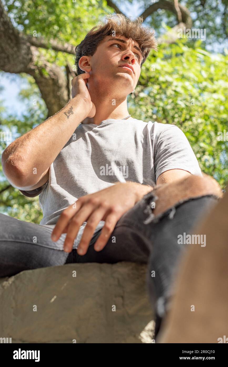 Ein junger Mann, ernsthaft, sitzt auf einem Baum und blickt weg Stockfoto