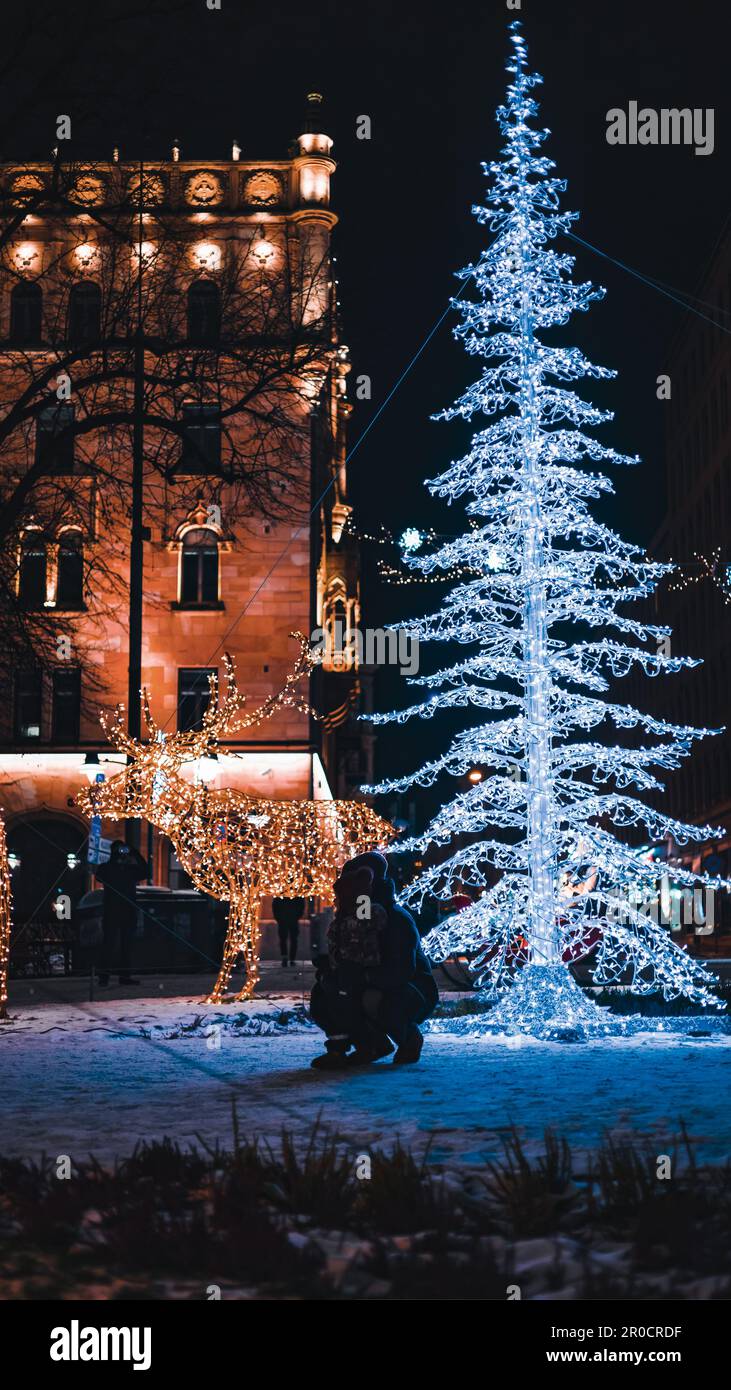 Eine festliche Winterszene mit einer Familie, die im Winter bei Nacht vor dem hellen Weihnachtsbaum Spaß hat Stockfoto