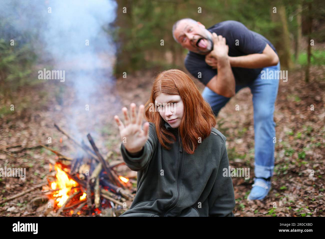 Eine junge rothaarige Hexe mit einer magischen Hand und ein alter Mann auf dem Rücken beginnen, vor einem Fluch zu sterben Stockfoto