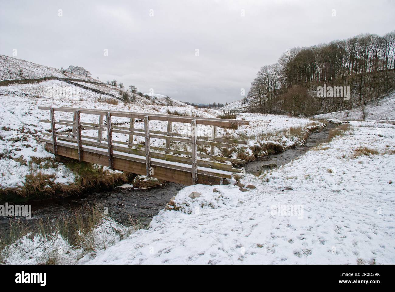 Schneeszene mit Holzbrücke über dem Long Preston Beck im Yorkshire Dales National Park. Stockfoto