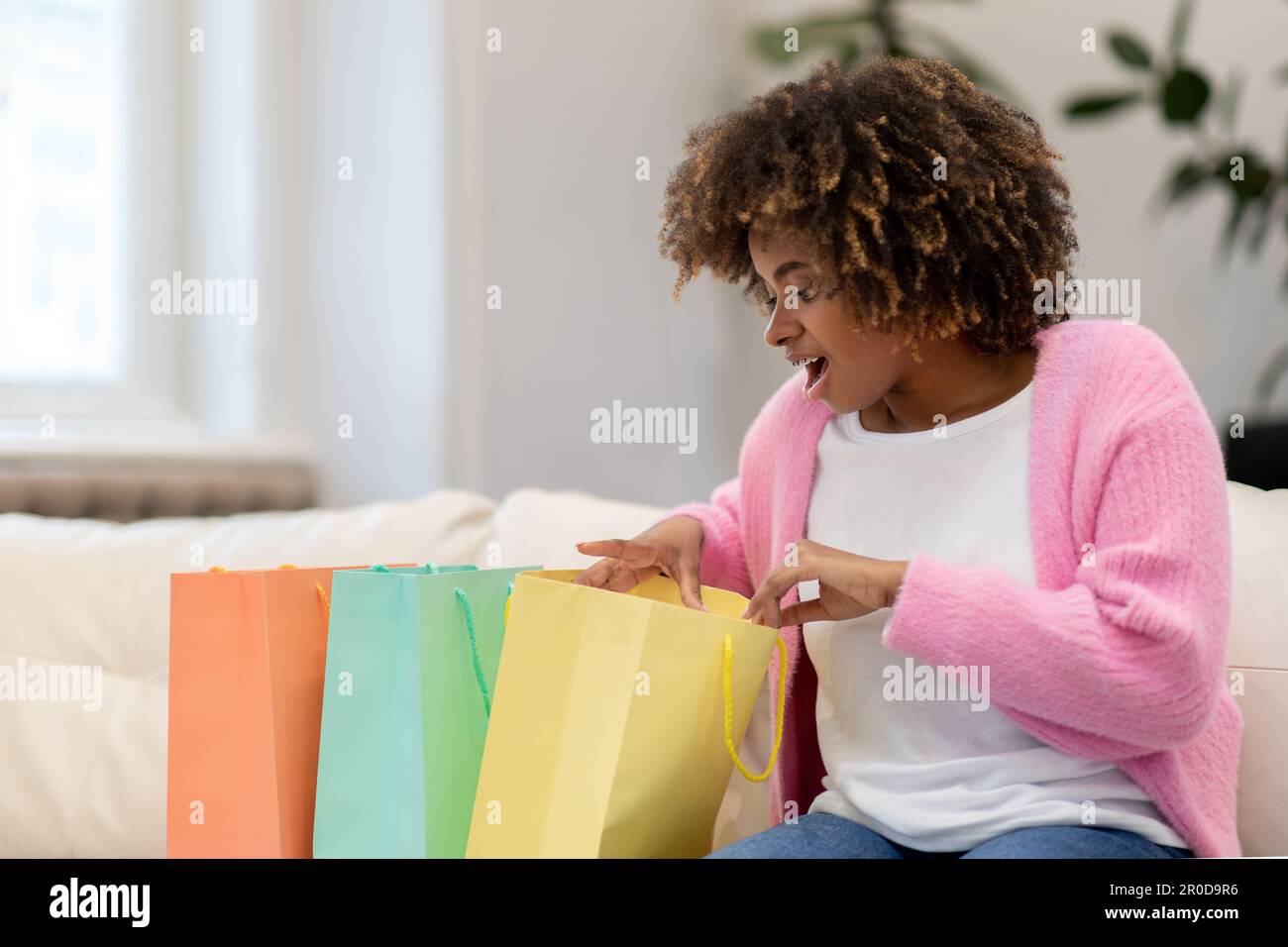 Aufgeregte afrikanerin, die zu Hause bunte Einkaufstüten überprüft Stockfoto